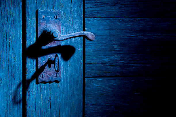 Old wooden door with rusty vintage lock set with skeleton key and lever door handle. High side lighting with blue gel to simulate street lighting. Horizontal format with room for text.