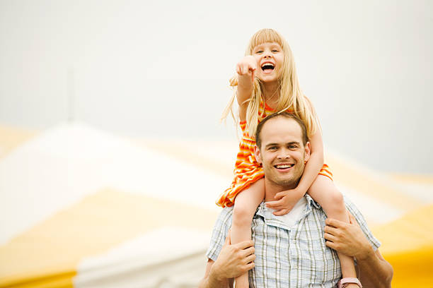 Father and Girl Child on Shoulders at Fair or Circus stock photo