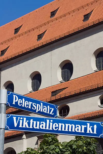 "Munich Street Sign: Petersplatz and Viktualienmarkt (The famous ""Victuals Market"" in the centre of Munich). In the Background the Church ""St. Peter, called Old Peter - the oldest parish church in Munich, Upper Bavaria, Bavaria, Germany). Selective Focus. Focus on the street sign."