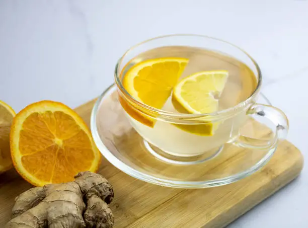 A cup of fresh ginger root tea with lemon and orange slices.