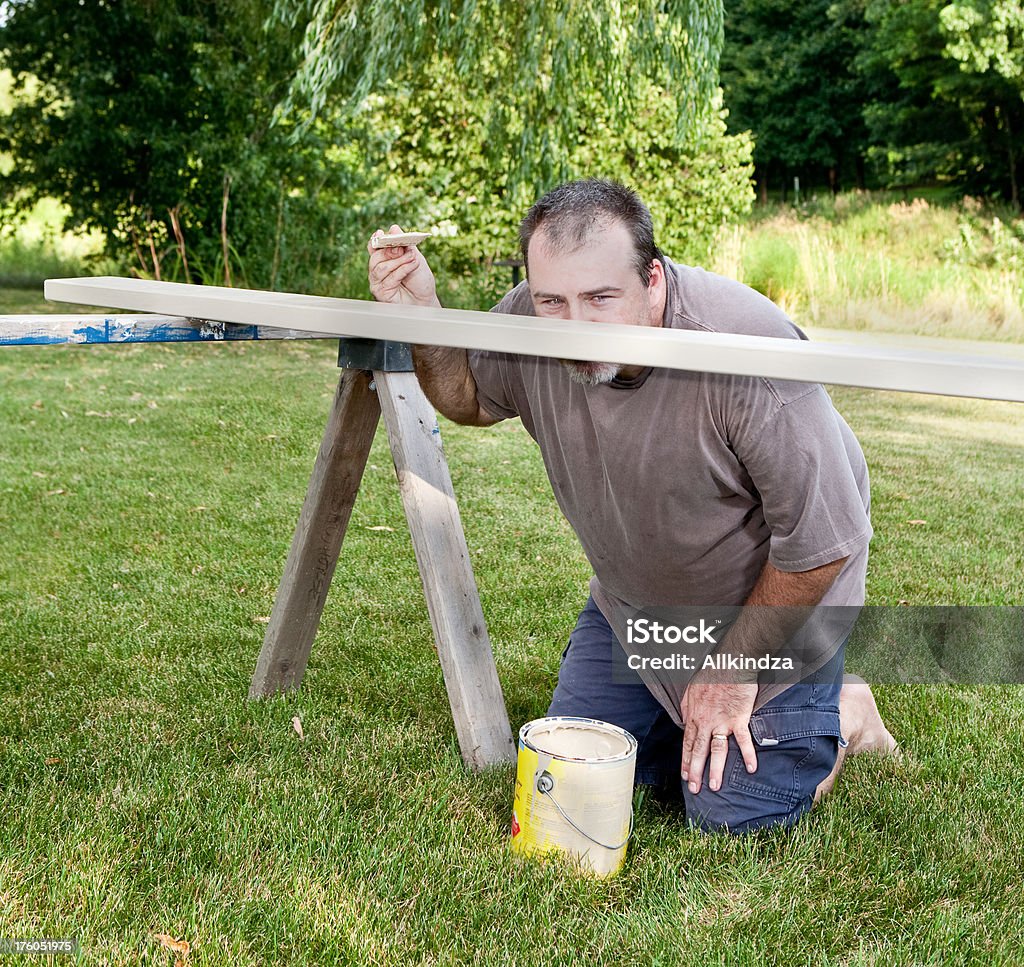 inspecting the paint job a middle age man kneels and looks very close at the paint job he is doing. Adult Stock Photo