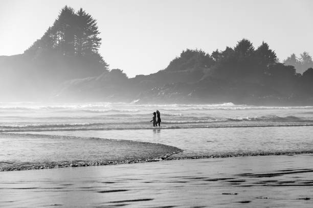 Two women walking in the Pacific Ocean waves at Cox Bay Beach, Tofino, Vancouver Island, British Columbia.