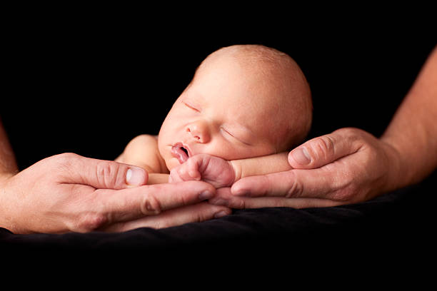 istock Newborn Baby Sleeping in Father's Hands, Isolated on Black 176052765