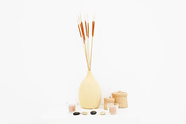 Spa equipment, basket, stones, candles, vase, brightly lit against white. Copy space.