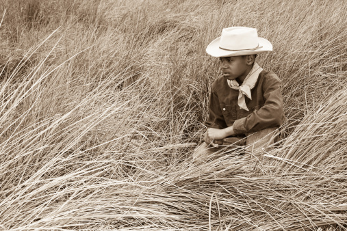 young cowboy crouched in a field of grasses