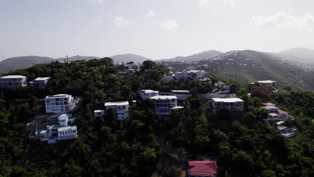 Aerial drone wide zoom out shot revealing homes on the hill and mountains in the background st. thomas coki beach sapphire beach turquoise water waves blue sky white clouds east end red hook hills