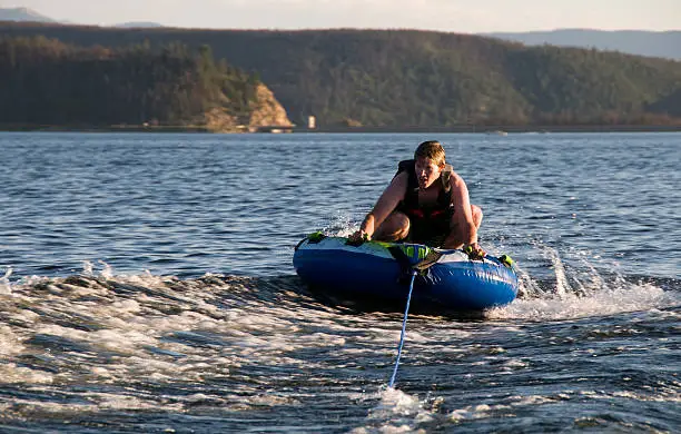 young man riding an inflatable inner tube towed behind a boat.