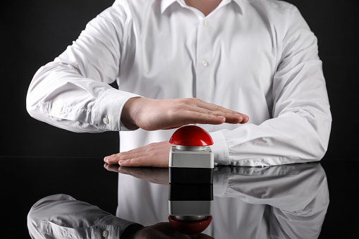 Man pressing red button of nuclear weapon on black background, closeup. War concept