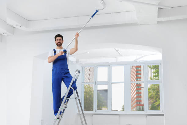 istock Handyman painting ceiling with roller on step ladder in room 1760624404