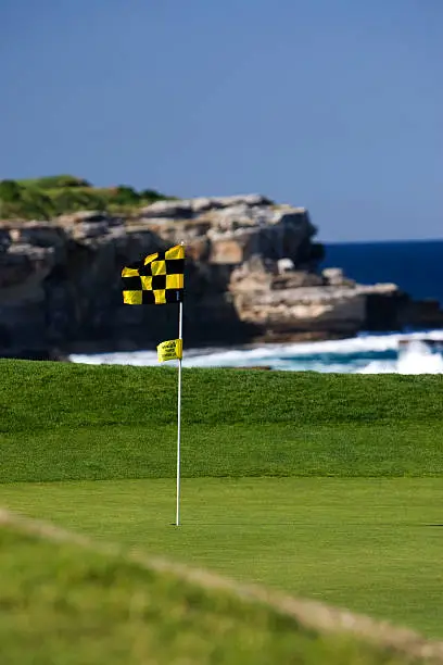 A golf flag blows in the wind on a beautiful golf course by the ocean with copy space.