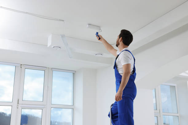 istock Handyman with roller painting ceiling on step ladder in room 1760624952