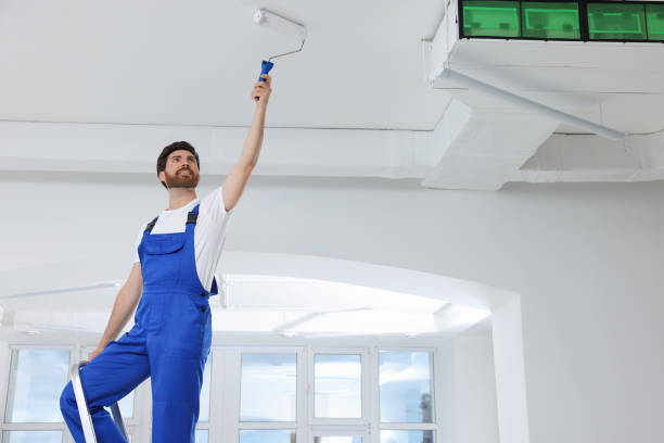 istock Handyman with roller painting ceiling on step ladder in room 1760624975