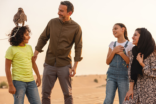 Family having fun and enjoying their time outdoors in the desert in Dubai. They are smiling at the daughter who has the falcon on her head.