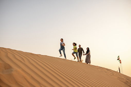 Family on vacation walking on the desert in Dubai. The children are running in front.