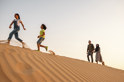 Middle Eastern young children are running in front of the parents in Dubai deserts.
