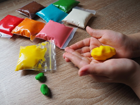 Classes with plasticine. Children's hands crumple soft plasticine. Packages with plasticine are on the table. Creativity for the development of fine motor skills of hands. Creating from plasticine.