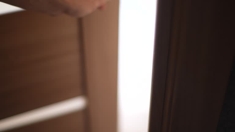Close-up unrecognizable male hands opens door in dark room and walks into room with light interior. Close-up cropped shot of young man takes door knob