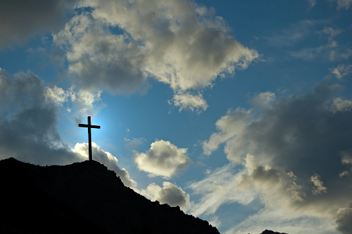 A crucifx on the top of a mountain peak with a setting sun... backlighting.
