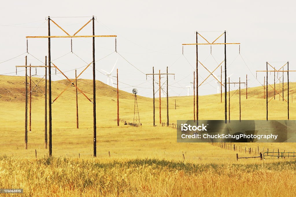 Electrical Power Windmill Technology Energy Progress "Electrical power pylons with both old and new windmill technology in the background spreading across a rural Midwest landscape in Summer heat compressed using a long lens.  One old windmill representing obsolete technology, many electrical pylons representing the current state of energy, and a handful of cutting edge wind turbines representing our progress to date in new technology." Connection Stock Photo