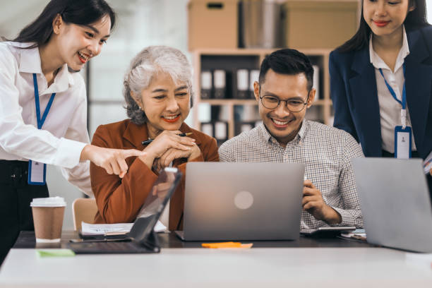 istock Four asian people in an office, working together on laptops, discussing tasks. annual gathering where attendees share and discuss opinions, presentation teamwork group meeting laptop in boardroom 1760646400