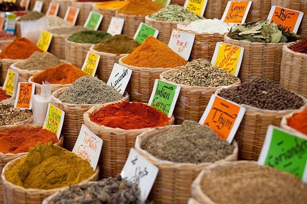 Wicker baskets filled with vibrant spices and herbs are displayed outdoors at a traditional Old Dubai market. The warm sunlight highlights the rich colors and textures, evoking the charm of Middle Eastern culture and trade.