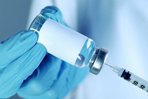 Laboratory worker filling syringe with medication from glass vial, closeup