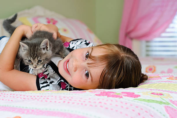 Young girl lies on her bed while holding a small kitten