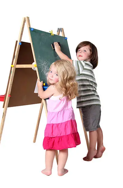 Barefoot brother and sister drawing on a chalkboard easel