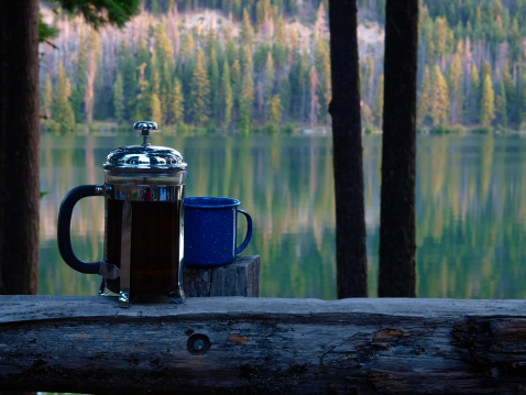 Early morning coffee steeping in a french press on railing overlooking sun rising on lake
