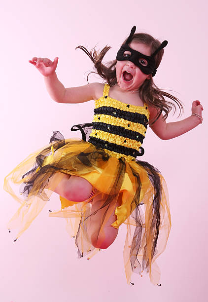 Jumping Bee A young girl in a fancy dress bee outfit laughing as she jumps on her bed in front of a pink background bee costume stock pictures, royalty-free photos & images