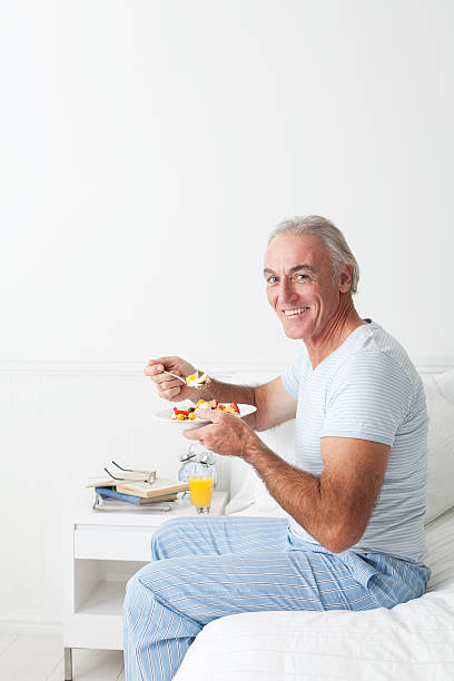Happy senior man eating breakfest Happy senior man eating breakfast in his sunny bedroom. cerial stock pictures, royalty-free photos & images