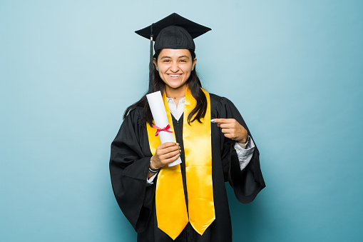 Smart attractive young woman pointing to her college certificate and smiling while graduating university looking excited