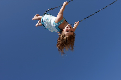 A little girl is swinging high against a blue sky. Low angle view. Plenty of copy space.