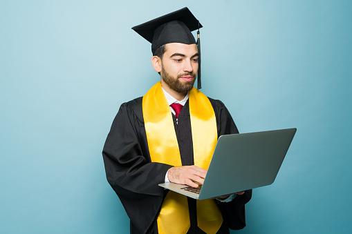 Latin smart college student using the laptop receiving his university degree after studying online and receiving his diploma