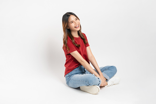 Happy smiling young woman sitting and shows hand pointing to the top, isolated on white background.