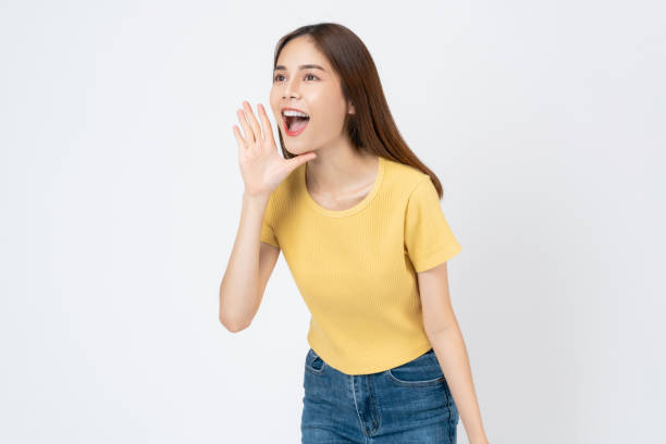 istock Young asian woman shouting and hands over mouth on white background studio. 1760757477