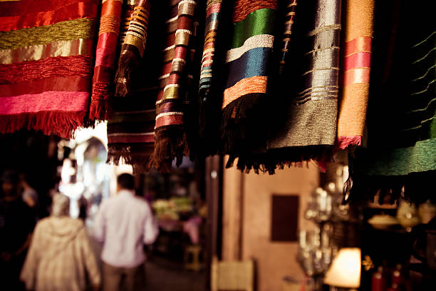 têxteis no mercado sobrelotado quadrado em marraquexe - craft market morocco shoe imagens e fotografias de stock