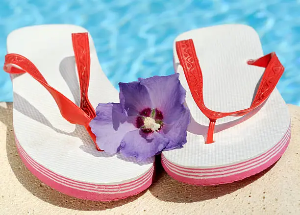 Sandals by a swimming pool with a hibiscus flower -  shallow DoF