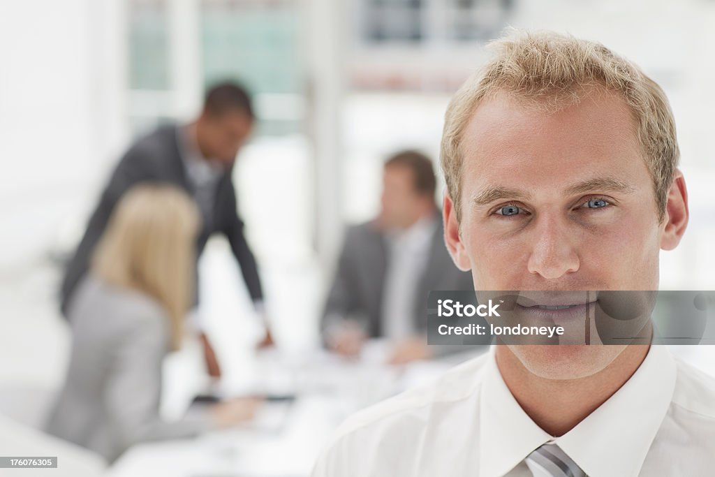 Handsome Businessman "Portrait of young businessman. In the background, his colleagues are having an informal meeting." Adult Stock Photo