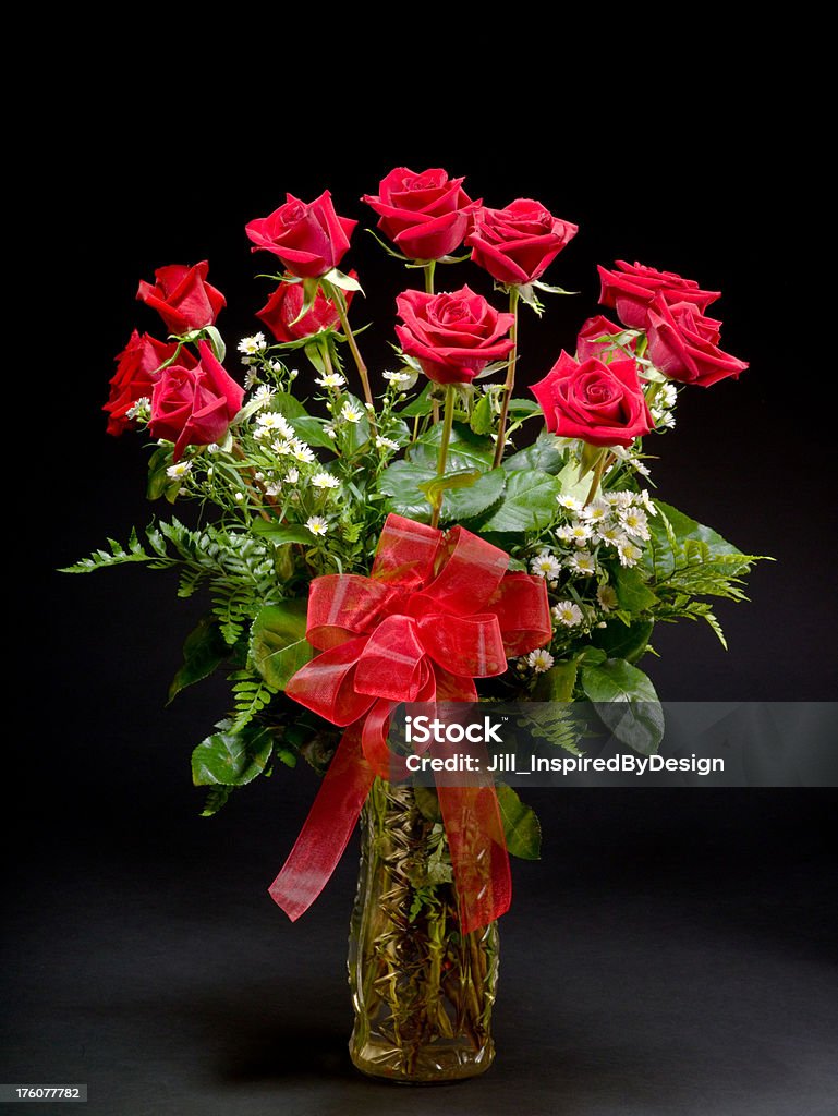 Dozen roses with black background One dozen red roses in front of a black background. Roses are in a glass vase. Translucent red bow is in the center. Vase Stock Photo