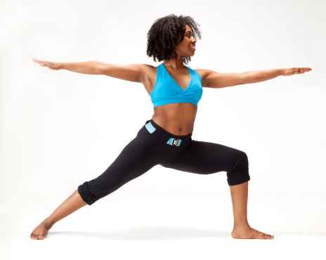 young African-American woman standing in yoga warrior pose dressed in fitness clothing on white background