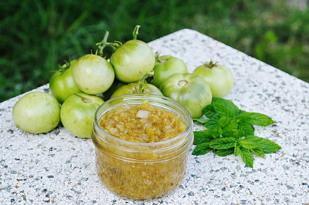 Green tomato paste along with green tomatoes Home-made green tomato chutney (green tomatoes, apples, onions, cider viengar, demerara sugar and mint). Taken outdoors on stone table with mint and green tomatoes in the background relish stock pictures, royalty-free photos & images