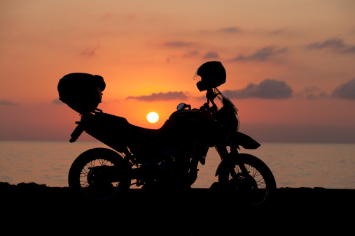 Silhouette of motorcycle on the beach. Beautiful sunrise at the background.