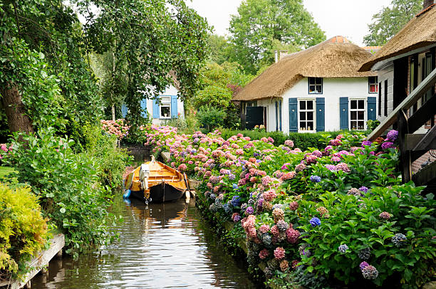 historic dutch houses with river, boat and many flowers - huisje stockfoto's en -beelden