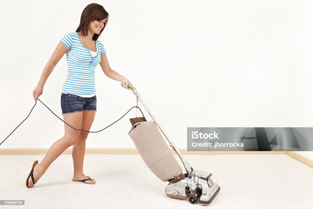 Young Woman Pushing Vacuum Cleaner "Photo of an attractive young woman in Tshirt and denim shorts, pushing a retro style vaccuum cleaner on carpet." Cleaning Stock Photo