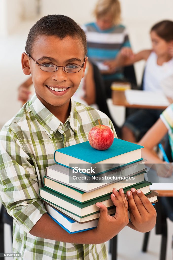 Smiling boy holding stack of books with an apple Smiling boy holding stack of books with an apple with friends in the background 8-9 Years Stock Photo