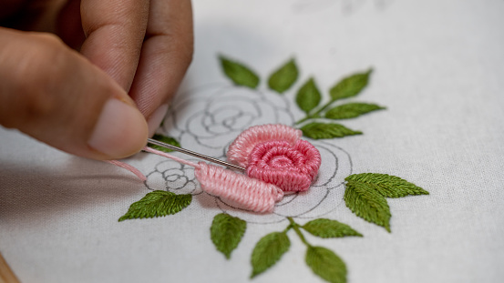 Hand stitching embroidery with a pink rose on a white background.