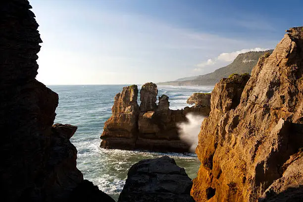 The cliffs of Punakaiki on the West Coast of New Zealand's South Island. Waves crash against the rocks sending plumes of spray skyward.