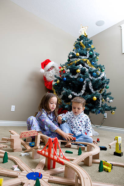 istock Two Children Play With Trainset While Santa Peeks Around Tree 176085559