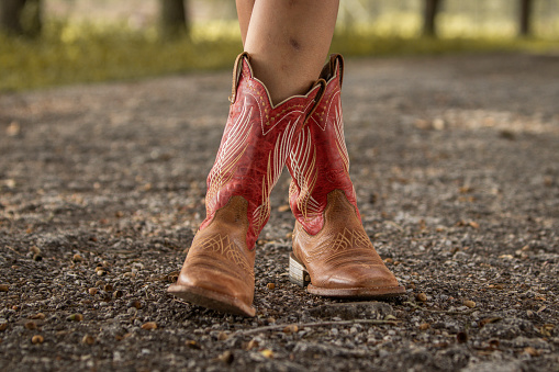 Woman wearing a pair of western boots while standing on a dirt road